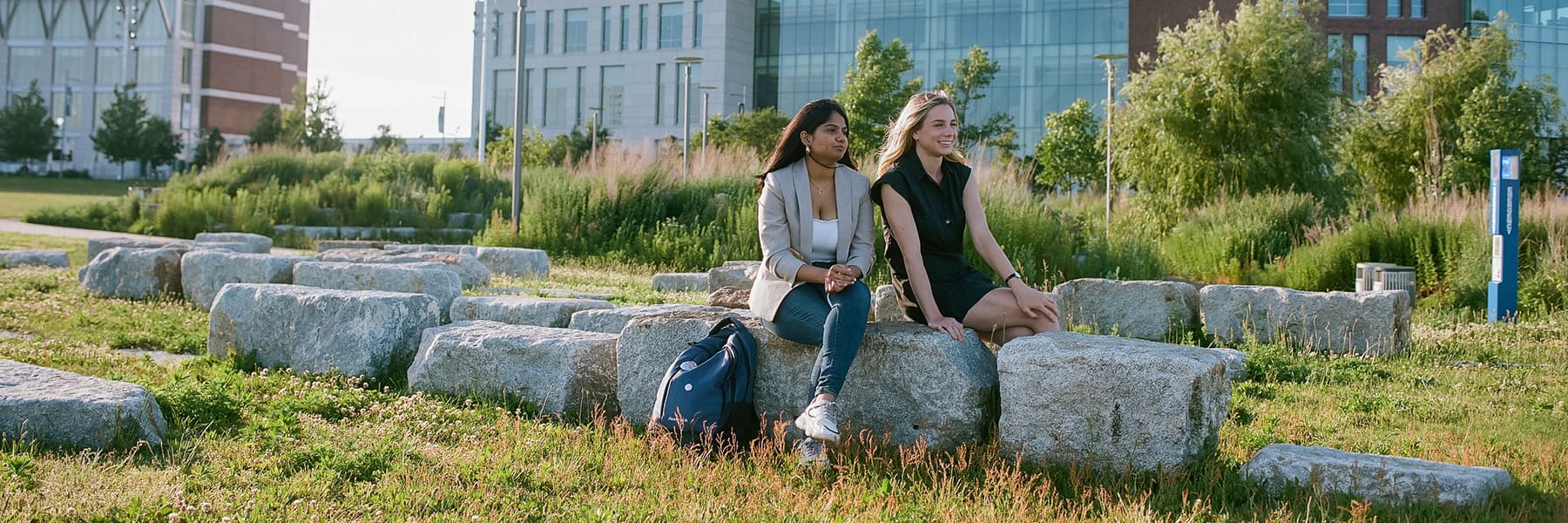 Two students sit on rock benches on campus center lawn.