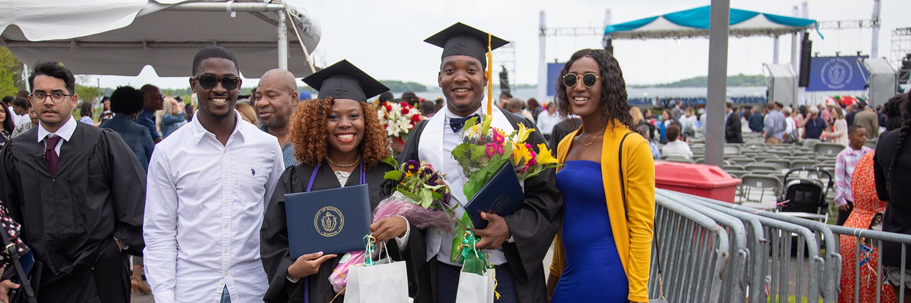 Students hold flowers standing with friends & families at Commencement.