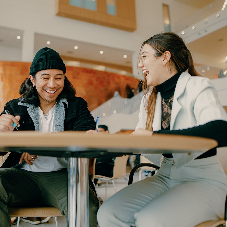 Two students talk at table in Uhall.