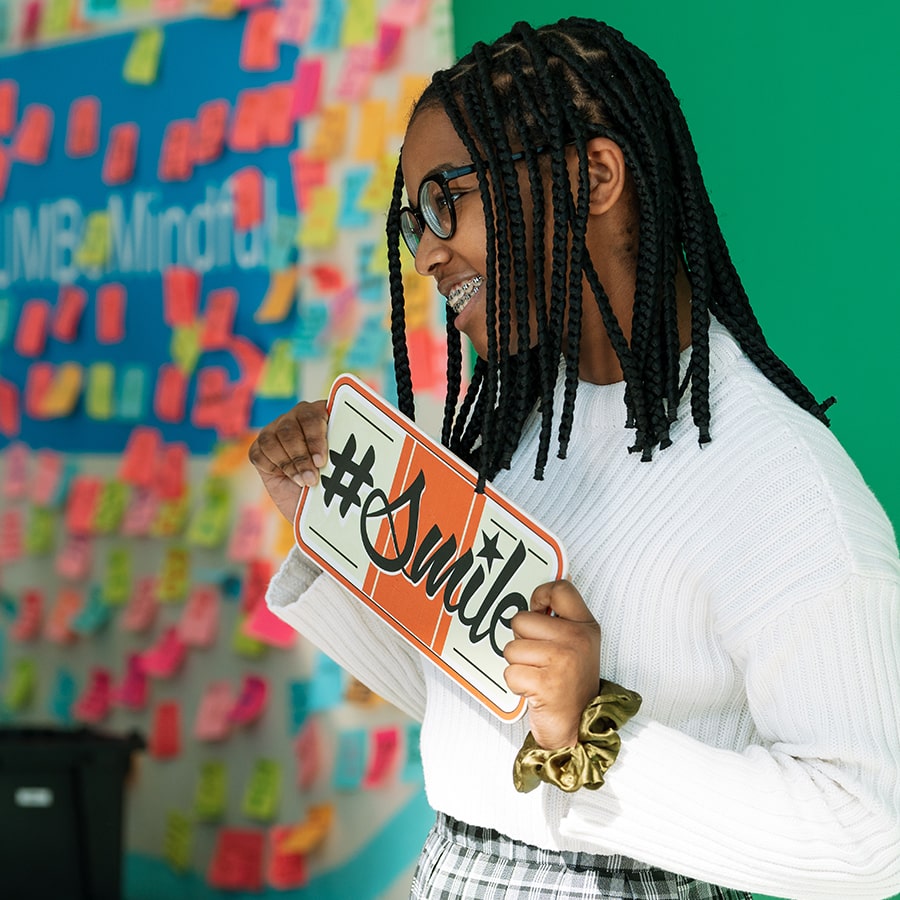 Student holds sign that says hashtag smile.