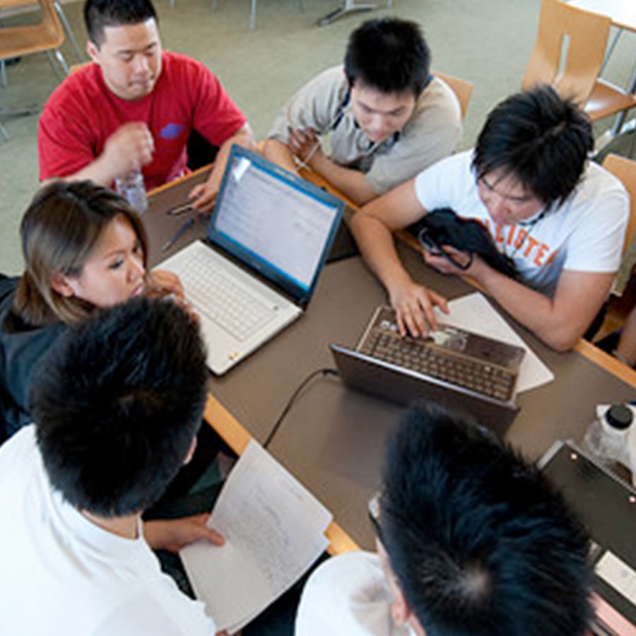 Group of students work on laptops in cafeteria.