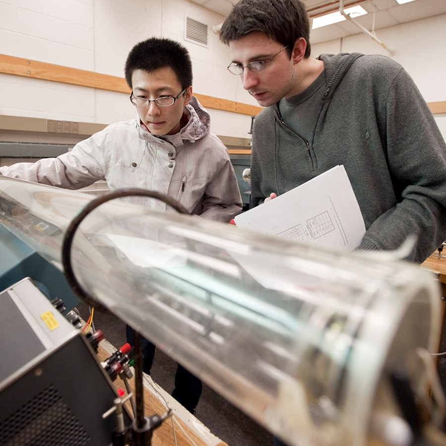 2 students work with a long tube in lab.