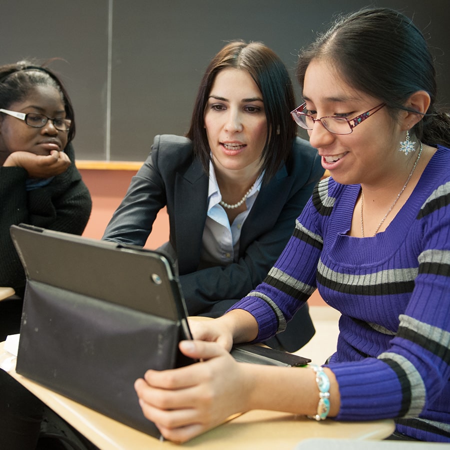 Faculty helps student on laptop in a classroom.