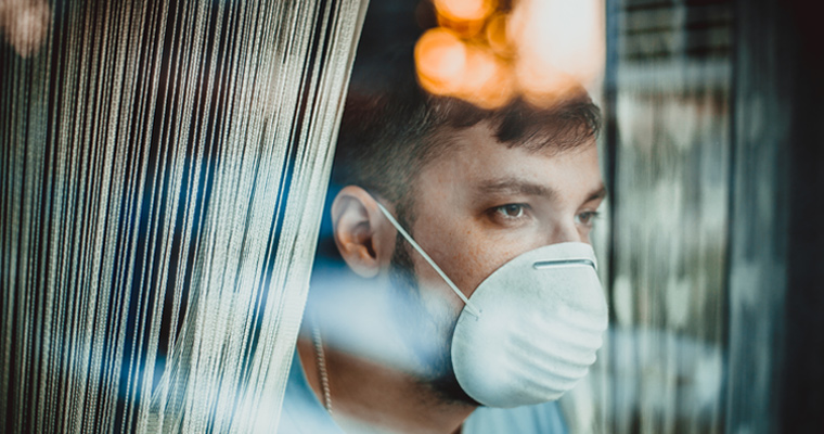 Man wearing a mask looking outside the window 