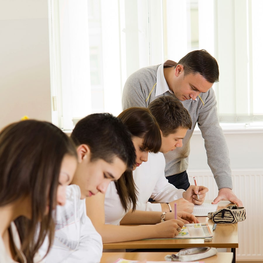 Teacher helping a high school student with a task in bright classroom.