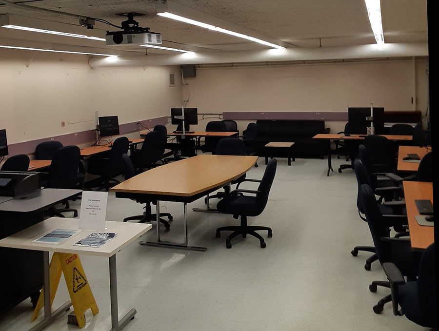 A lab with tables and chairs with desktop computers along the walls with a table and chairs in the center